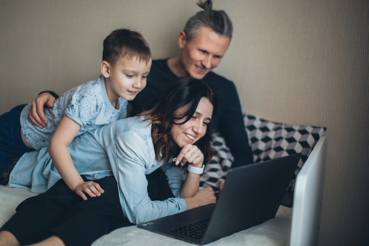 A person and person sitting on a couch with a child on her lap looking at a computer