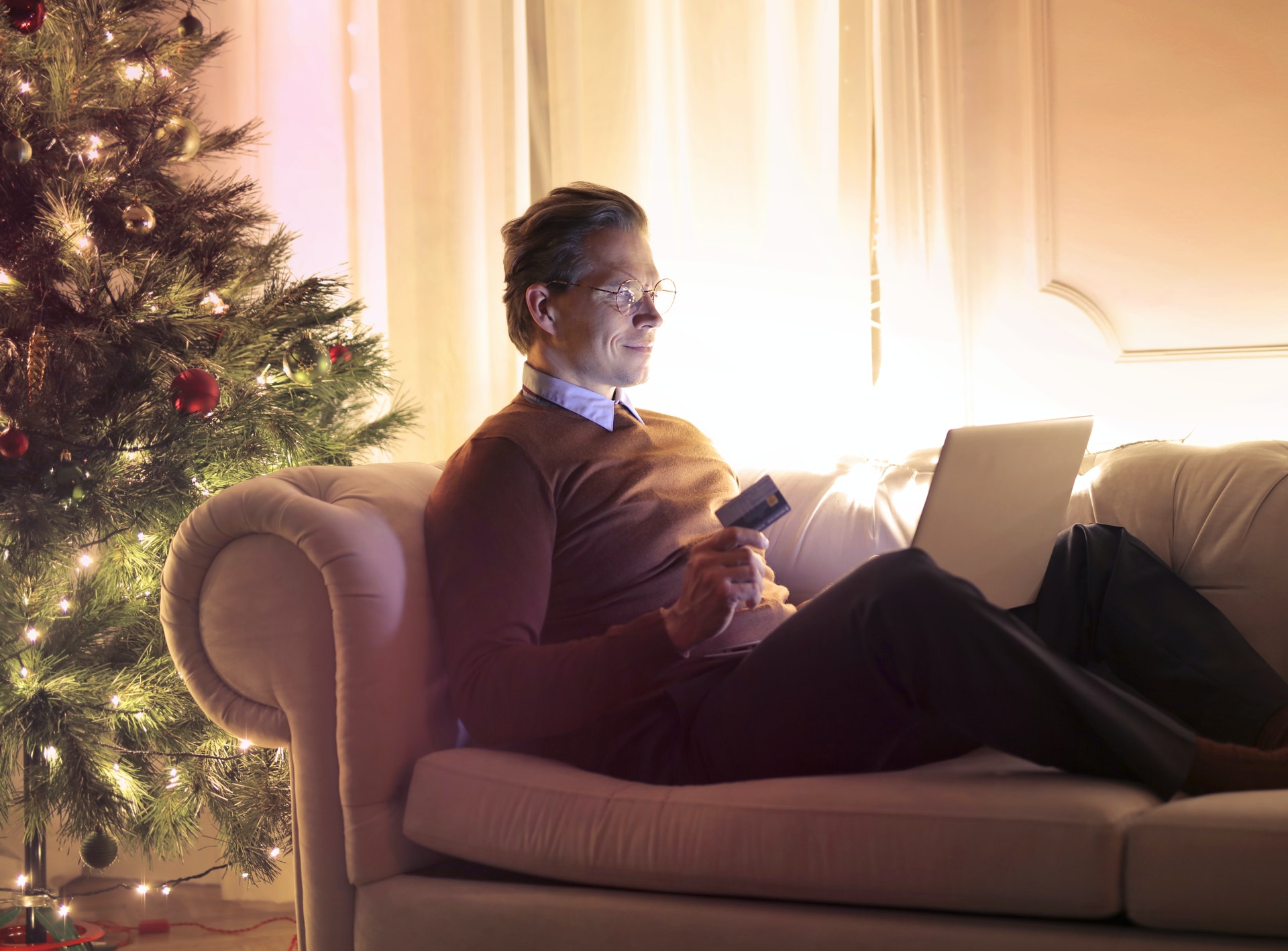 A person sitting on a couch with a computer and a Christmas tree